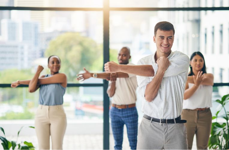 A group of diverse professionals actively participating in a guided movement session in a bright office environment, showcasing teamwork and wellbeing.